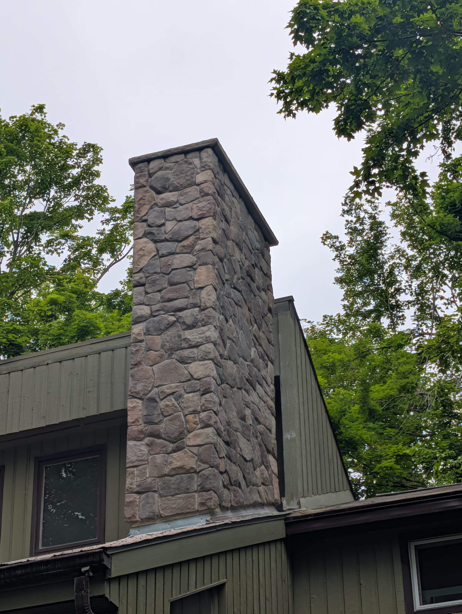 Stone veneer chimney with stone cap on a green chalet style house