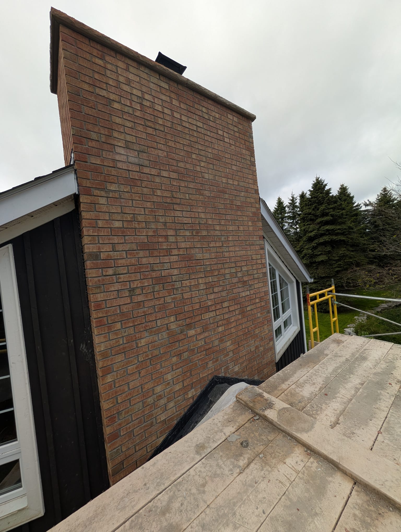 New buff brick chimney beside dark siding, photographed from scaffolding