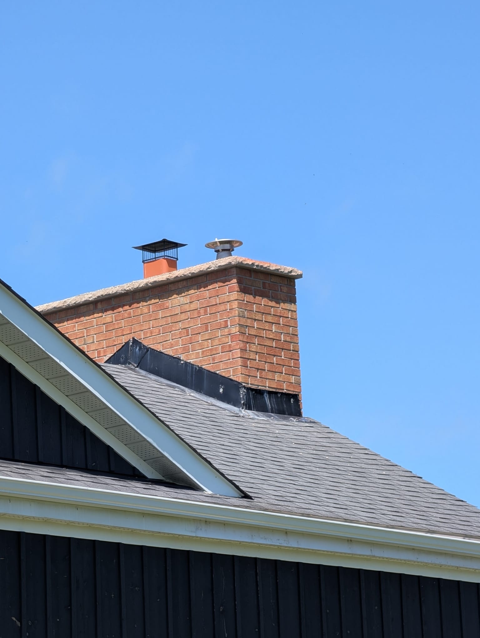 Brick chimney with new caps and flashing against dark siding