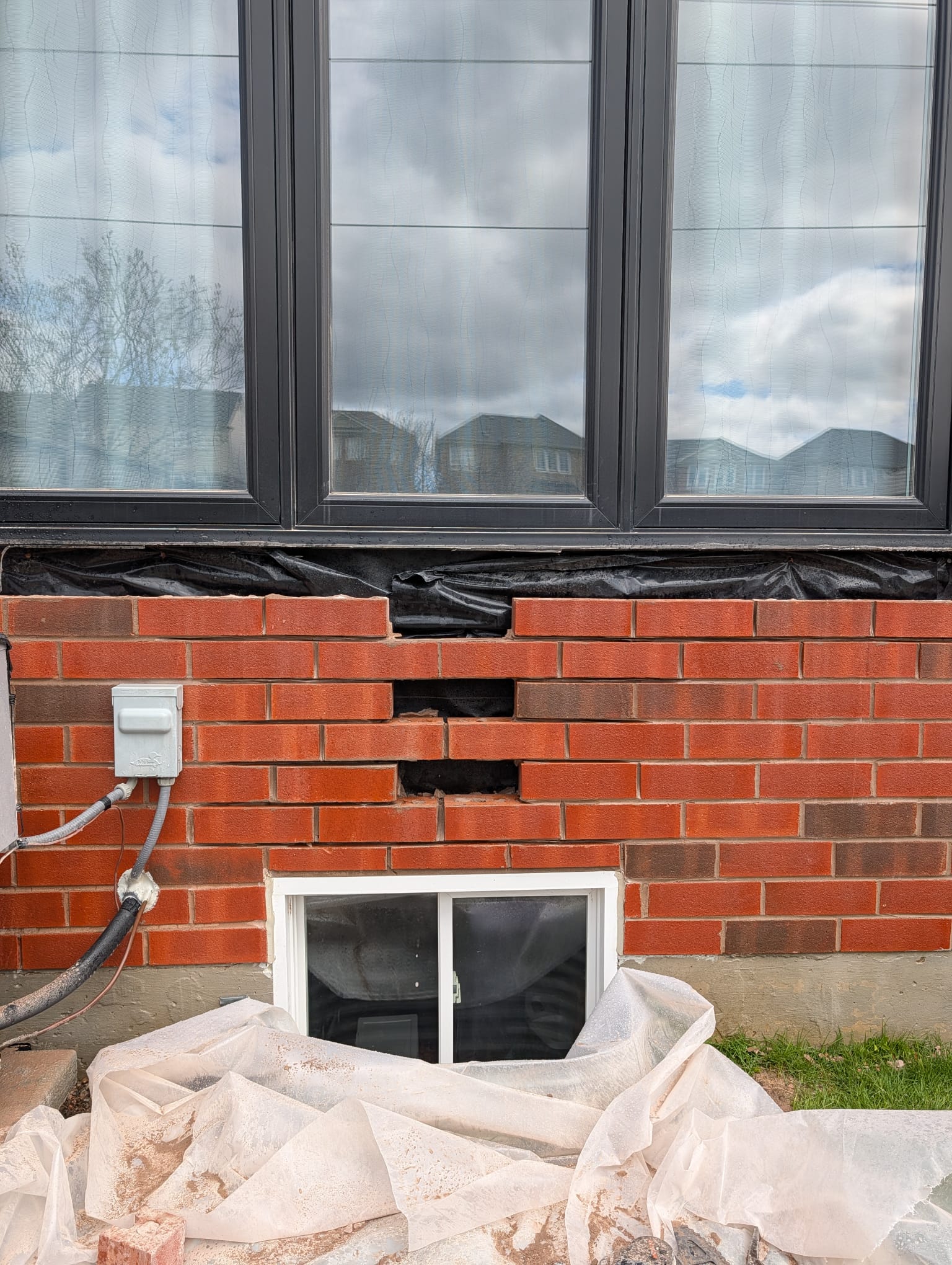 Wall with brick courses removed below windows showing membrane behind