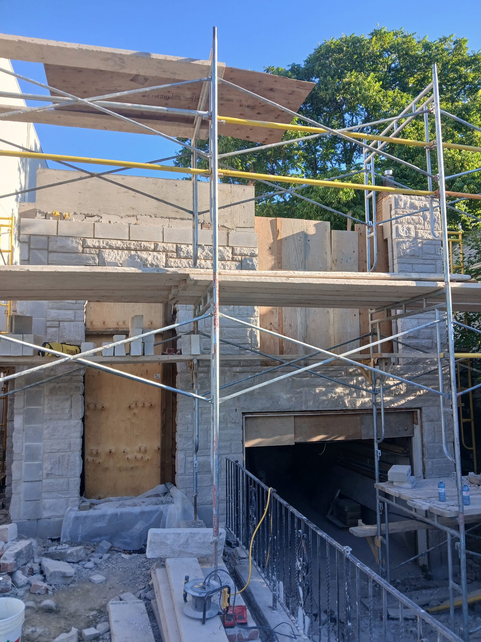 Two storey house in stone veneer with stone clad chimney behind full scaffolding
