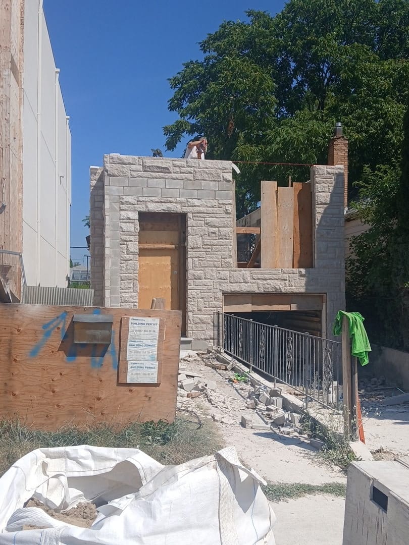Street view of a stone veneer build with permits posted on the hoarding
