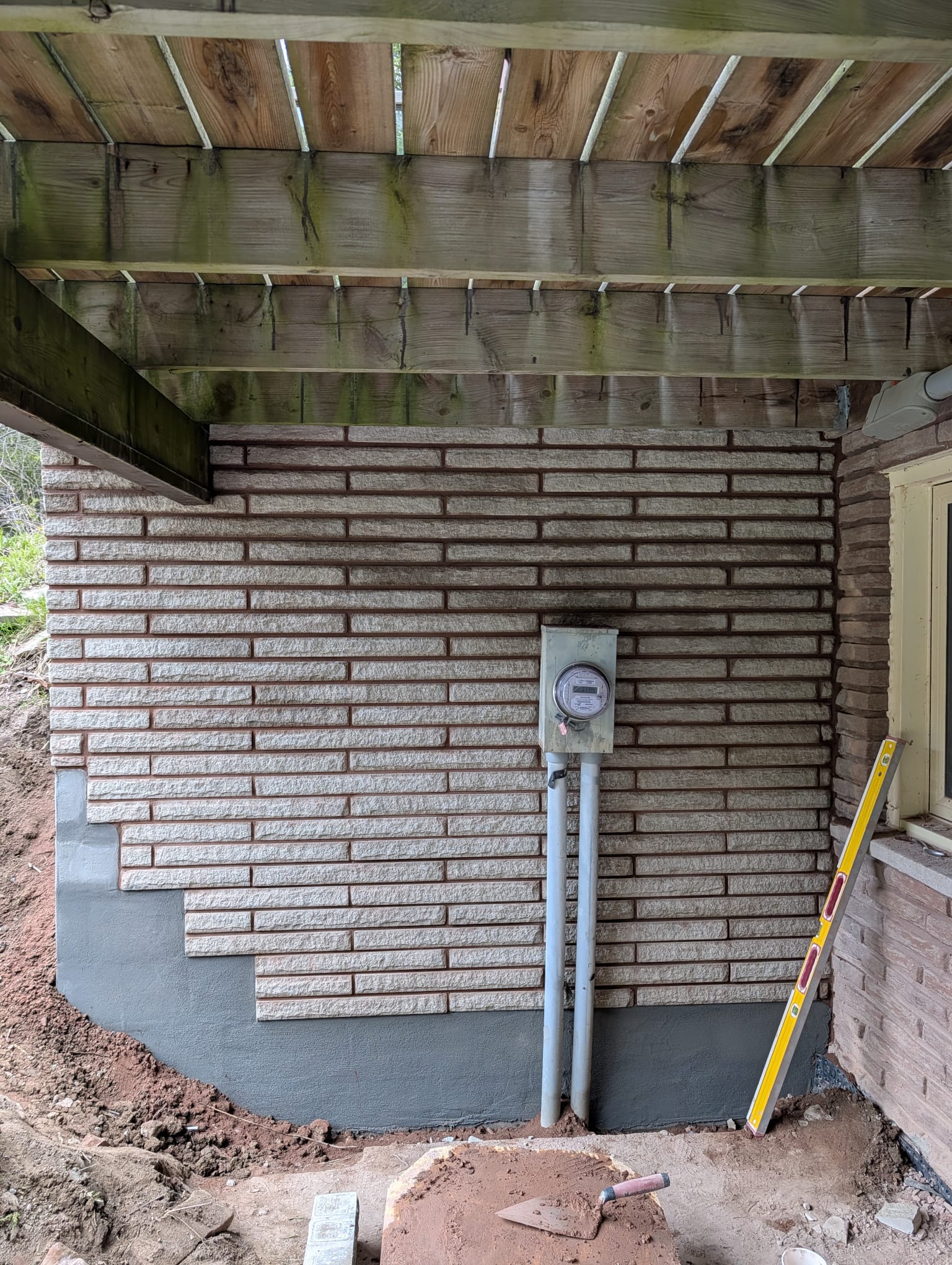 Fresh grey parging on a foundation wall with new stone refacing above, beneath a wood deck